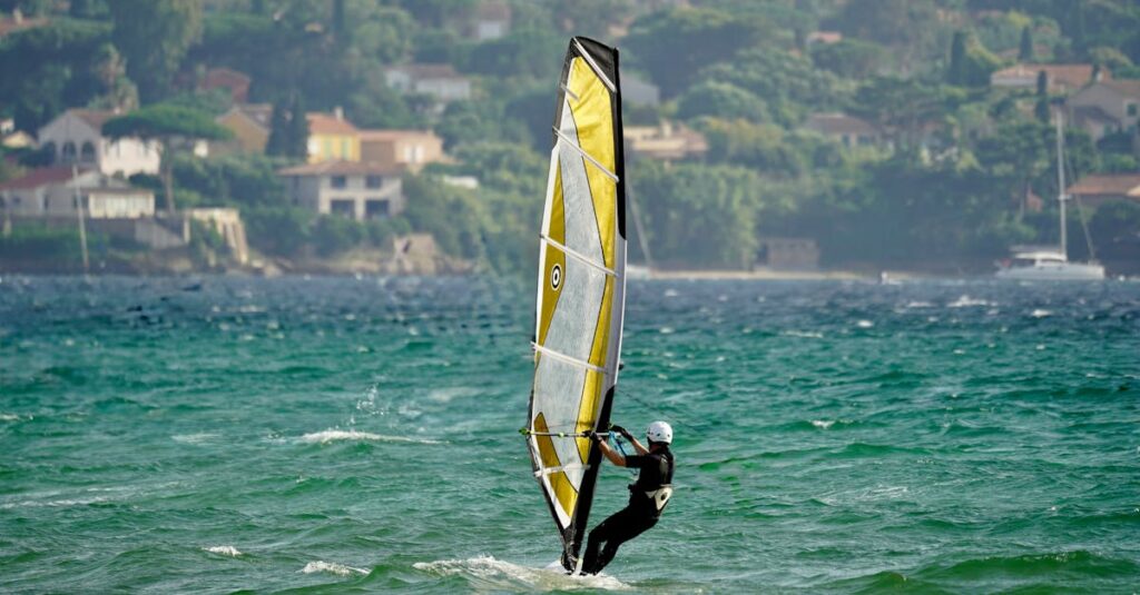 Windsurfer gliding over turquoise waves near scenic coastline houses.