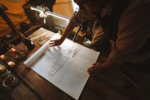 Two architects examine a blueprint by candlelight in a rustic setting, focusing on design details.