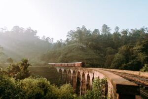 Scenic view of Nine Arches Bridge with train passing through lush greenery in Sri Lanka.