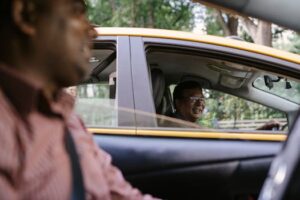 A candid street shot showing two men engaging in cheerful conversation while driving taxis in a city.