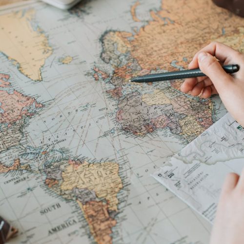 pexels-photo-7368308-7368308 Hands marking destinations on a world map surrounded by travel essentials like passport and camera.