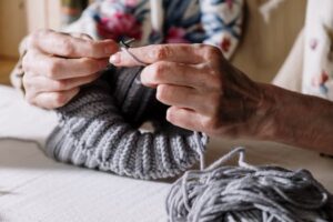 Hands engaged in knitting with grey yarn, highlighting the art of crochet and handmade craft.