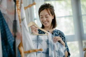 A cheerful Asian woman showcasing beautiful tie-dye fabric in a bright studio.