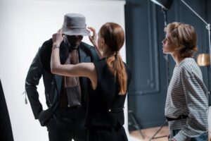 Fashion designers adjusting an outfit on a model during a studio photoshoot.